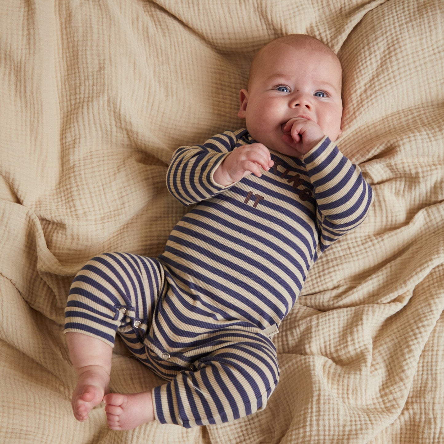 Baby in a striped onesie lying on a textured beige blanket