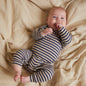 Baby in a striped onesie lying on a textured beige blanket