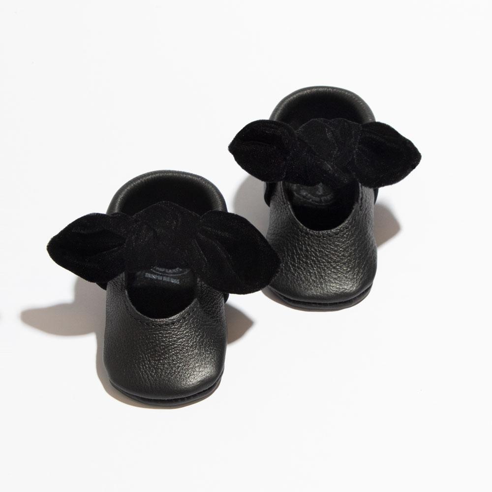 Pair of black baby shoes with velvet bows on a white background