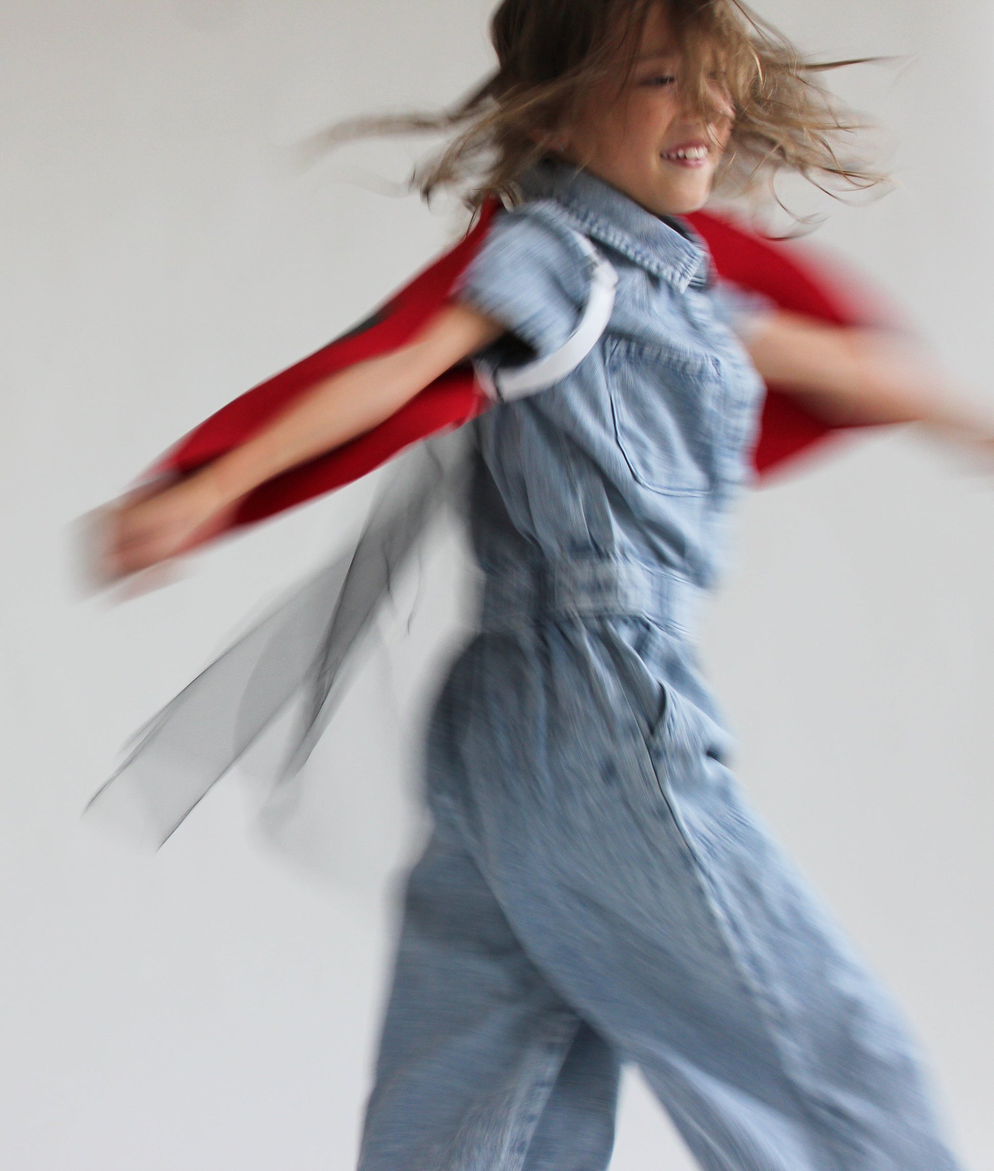 Child in a denim outfit with a red cape against a plain background
