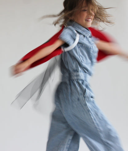 Child in a denim outfit with a red cape against a plain background