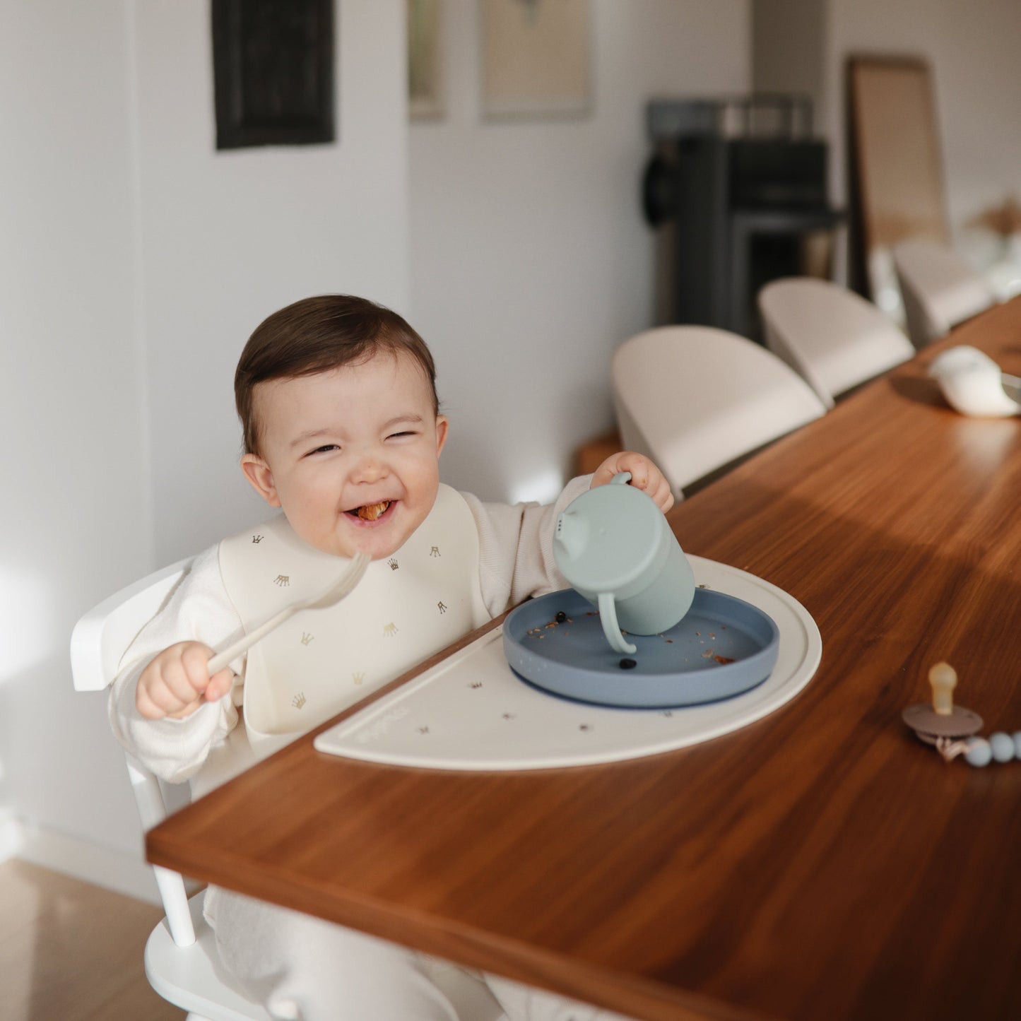 Baby sitting in a high chair with a blue sippy cup on a tray, smiling.