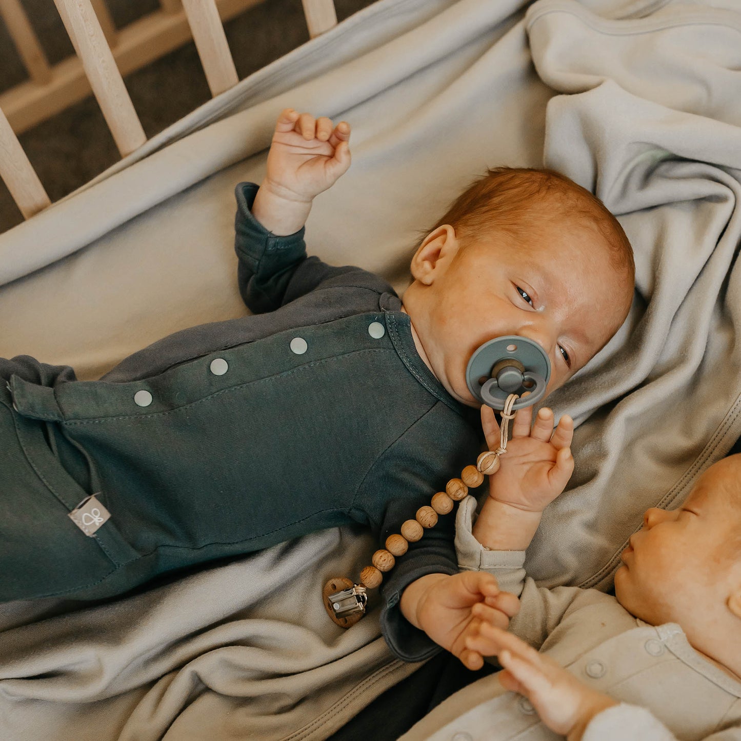 Baby lying in a crib with a pacifier, wearing a dark green outfit.
