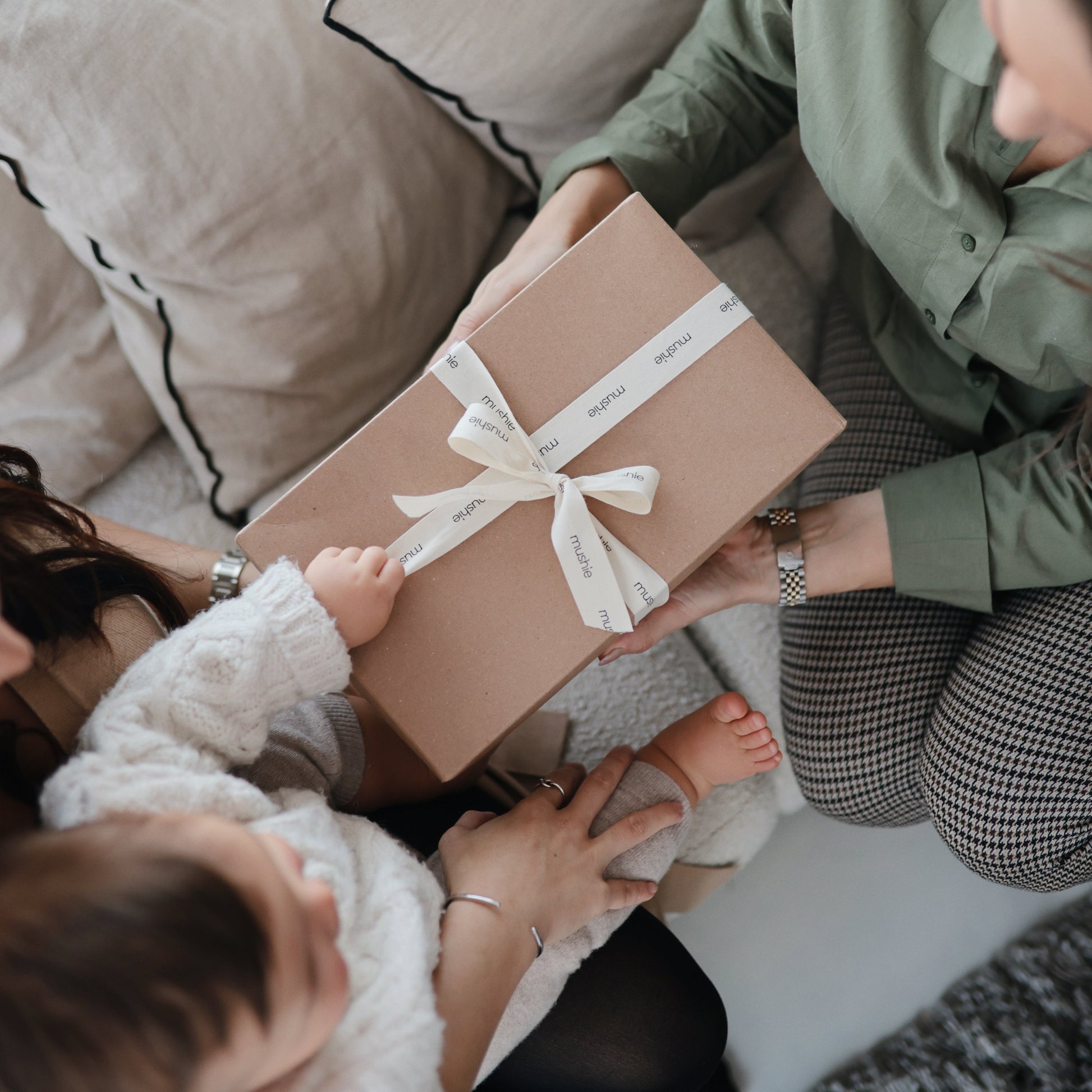 Two people exchanging a gift wrapped in brown paper with a white ribbon.