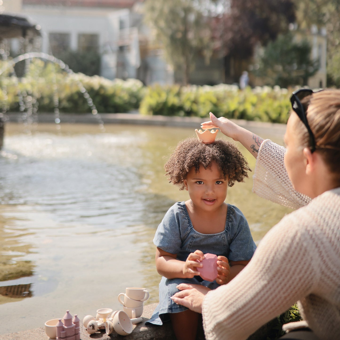 Woman and child playing with toys by a fountain in a park