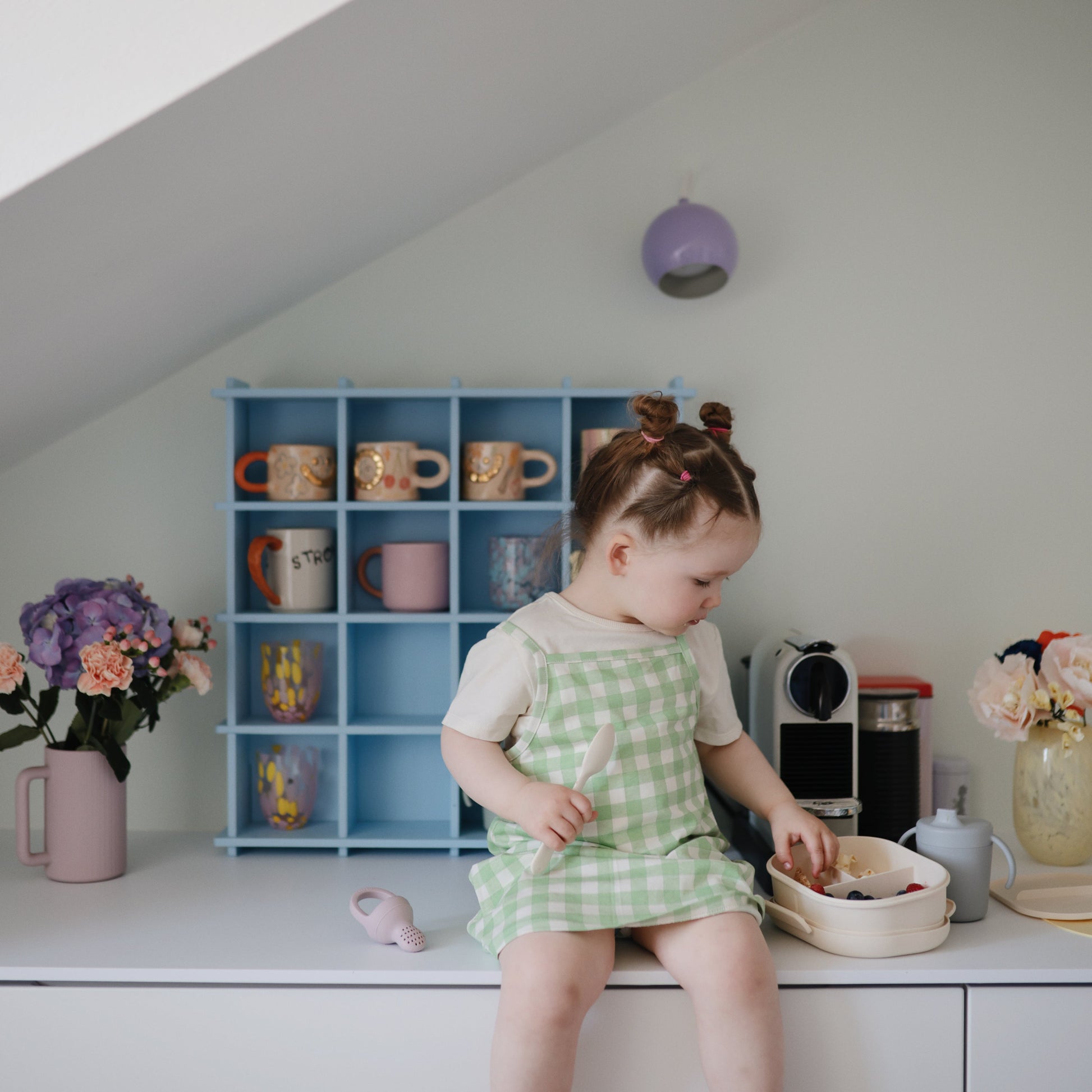 Child in a green checkered dress playing with toys on a white surface.