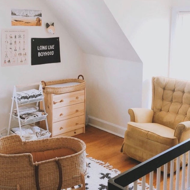 Nursery room with wooden dresser, wicker crib, and beige armchair.