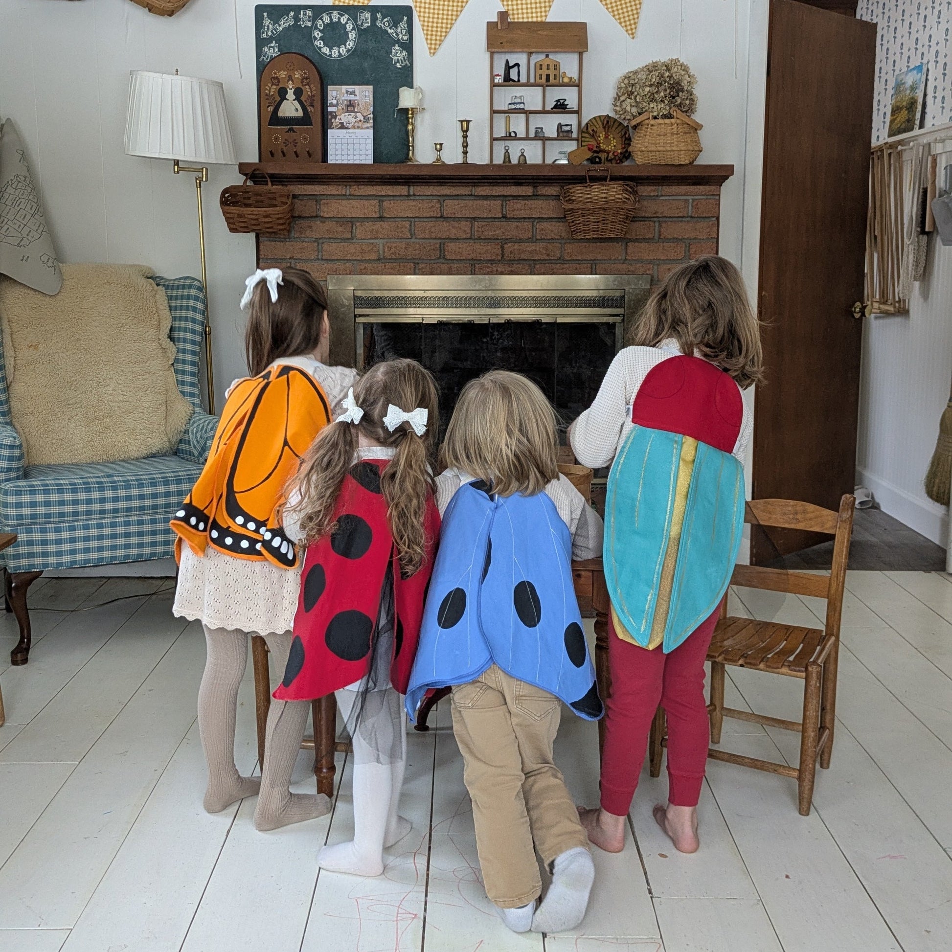 Four children in colorful costumes standing in front of a fireplace in a living room.