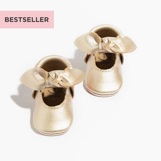 Gold baby shoes with bows on a white background, labeled as a bestseller.