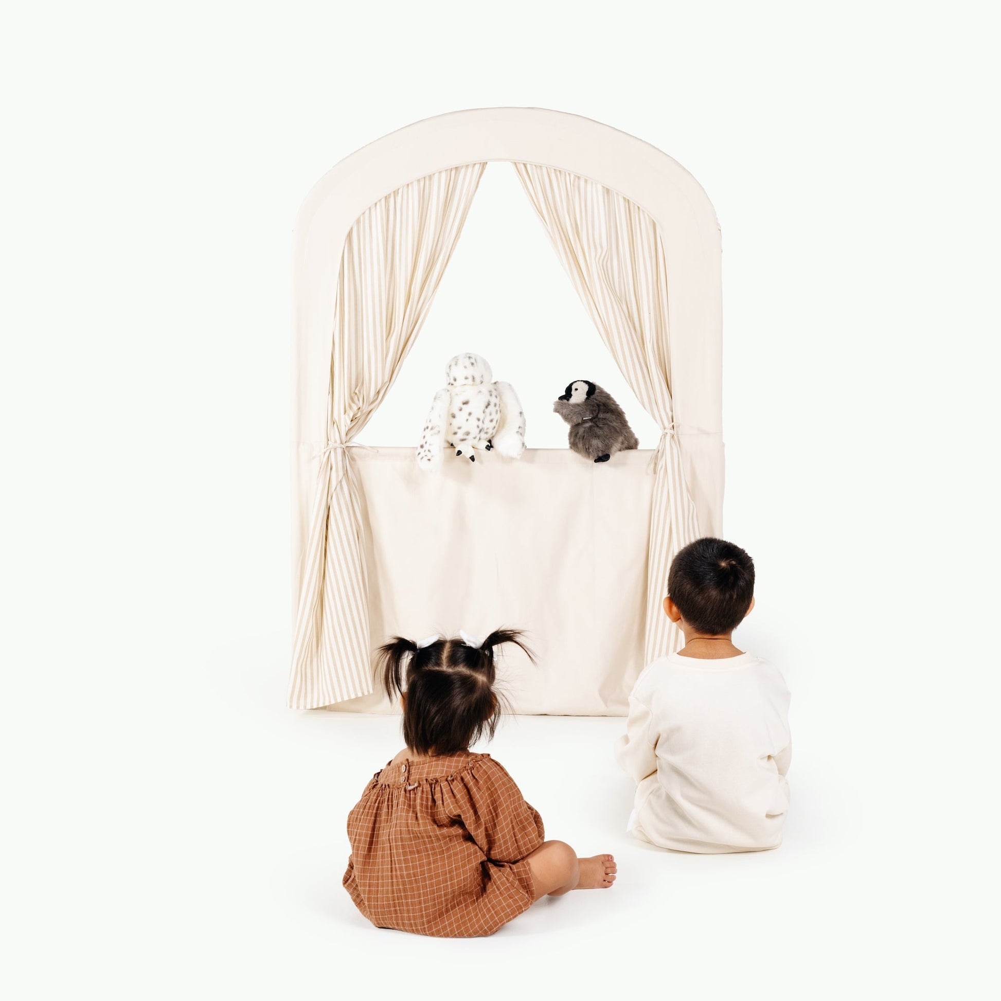 Two children sitting in front of a white curtain with a small dog on a white background
