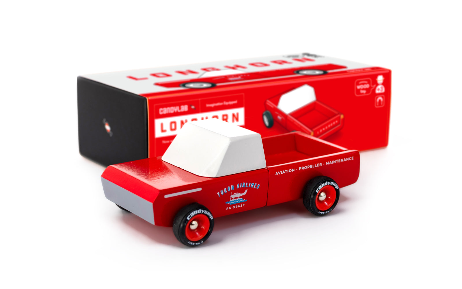 Red toy truck with white top and black wheels, displayed in front of its packaging on a white background.