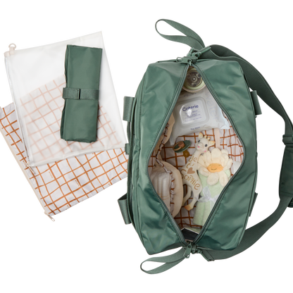 Green baby bag with baby items and a folded blanket on a white background