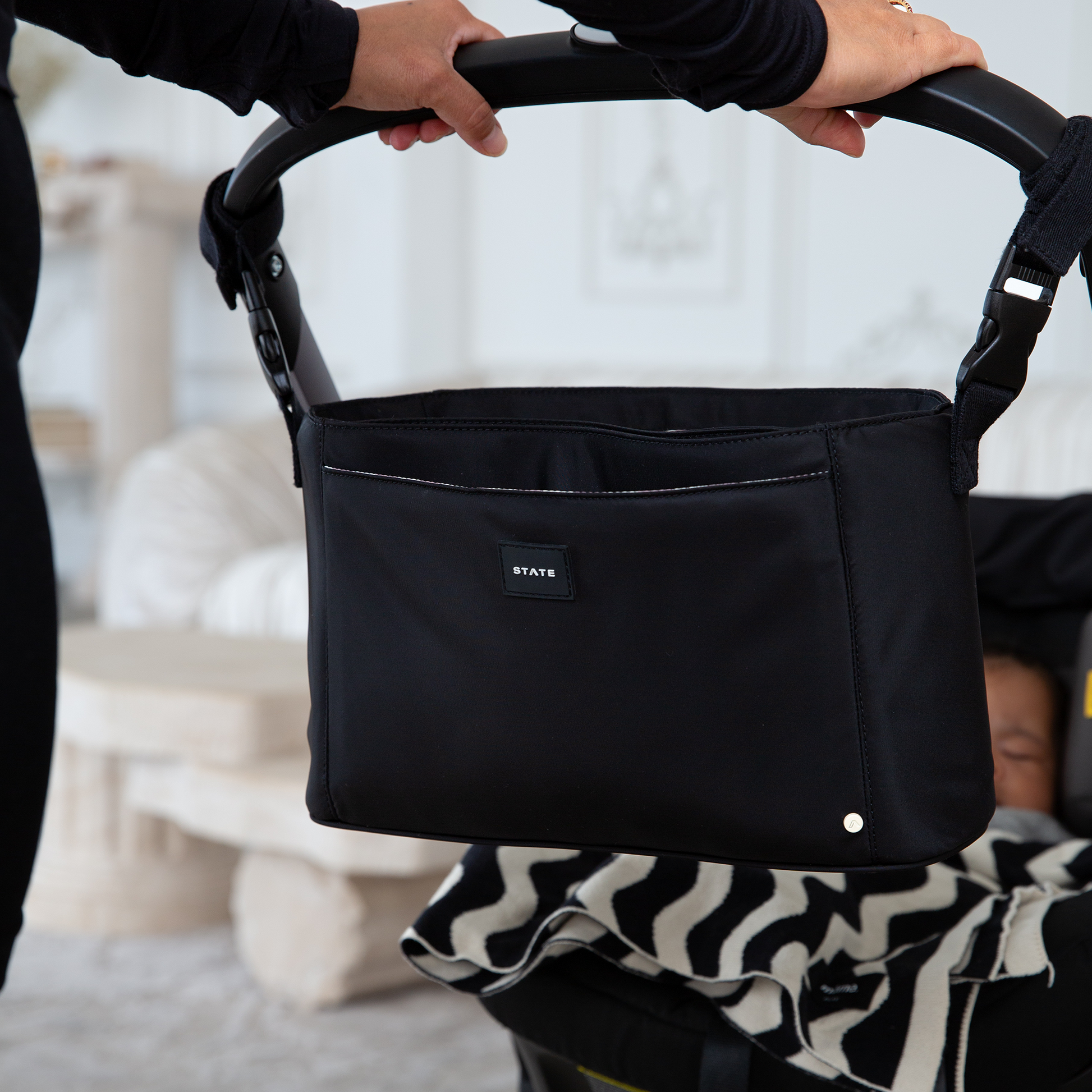 Black stroller organizer with 'STATE' label held by a person, blurred background