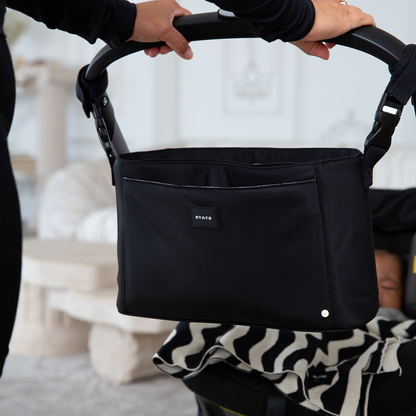 Black stroller organizer with 'STATE' label held by a person, blurred background