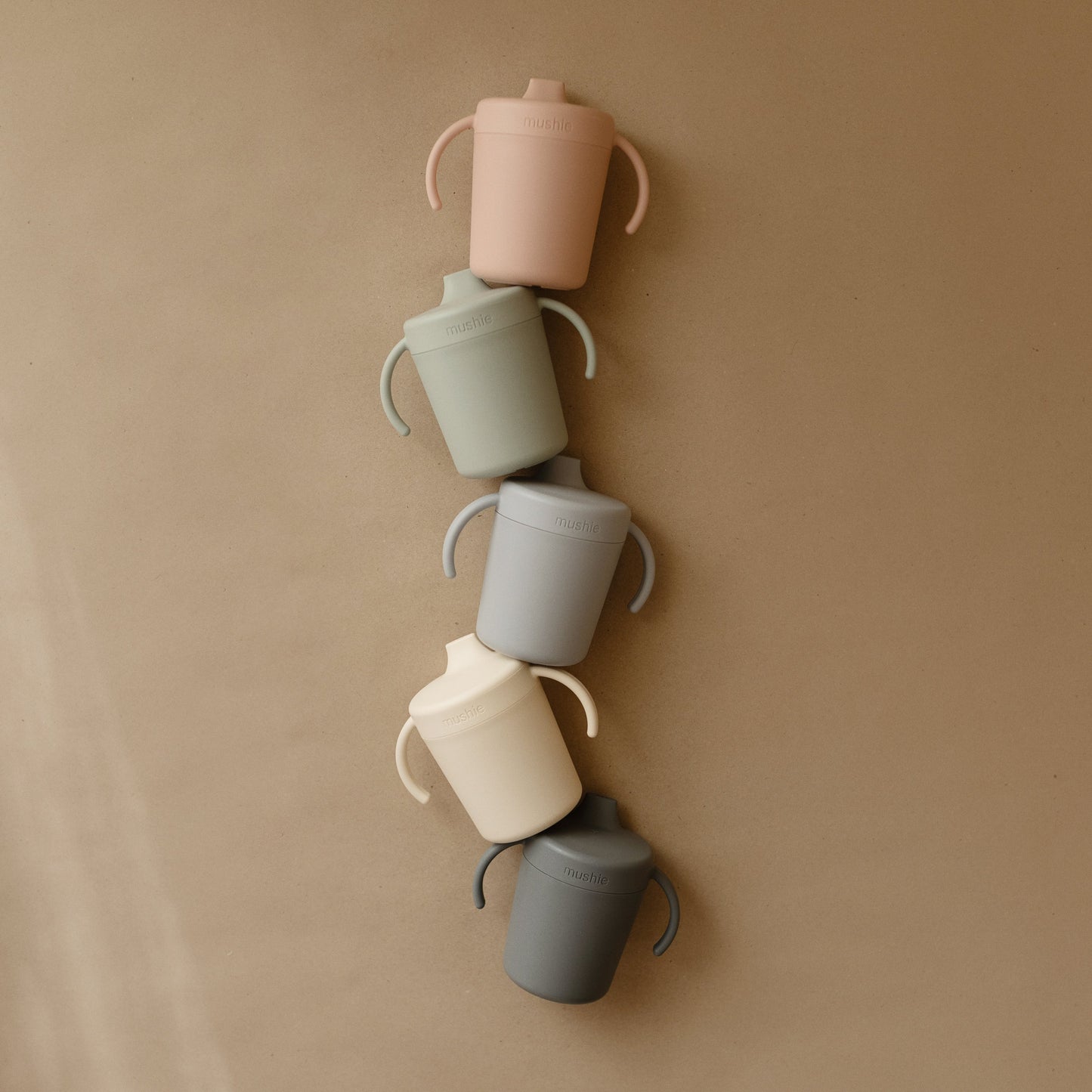 Set of colorful sippy cups arranged vertically on a beige wall.