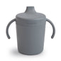 Gray sippy cup with handles and 'mushie' branding on a white background