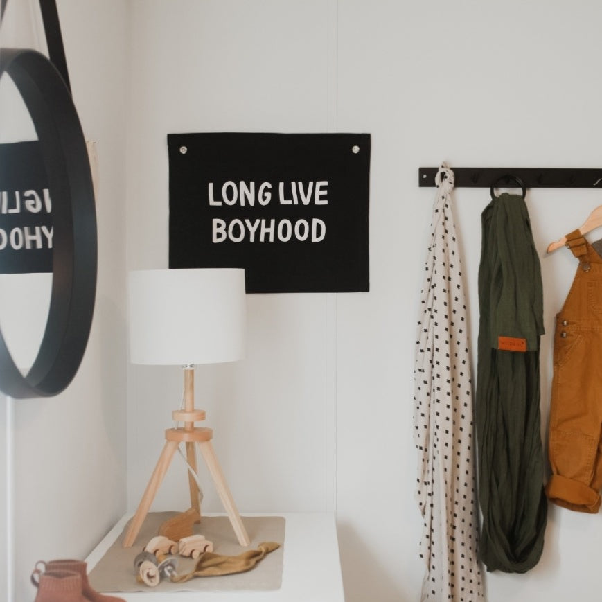 Decorative wall with 'LONG LIVE BOYHOOD' sign, lamp, and hanging clothes.