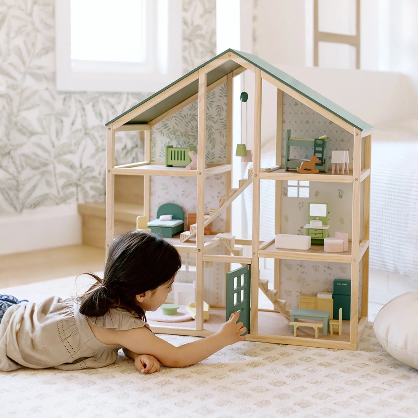 Child playing with a wooden dollhouse in a bright room.