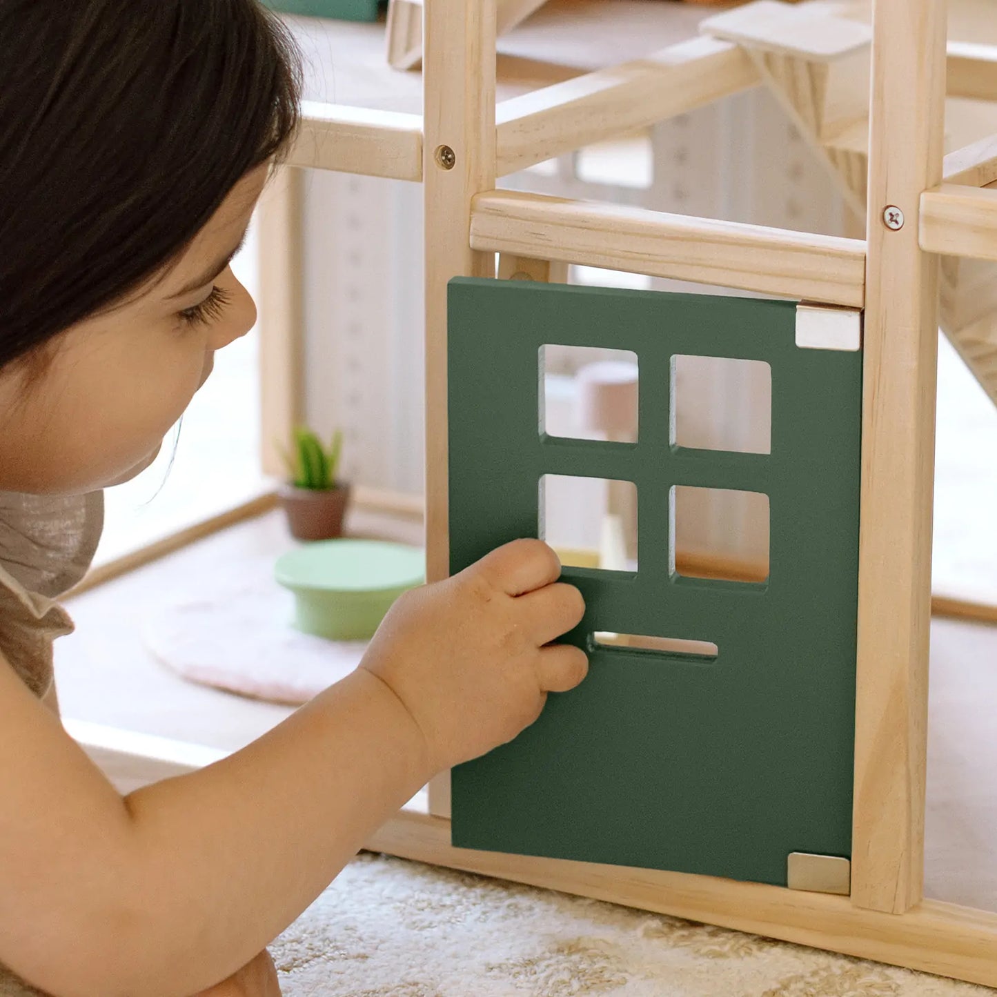 Child playing with a wooden and green toy structure indoors.
