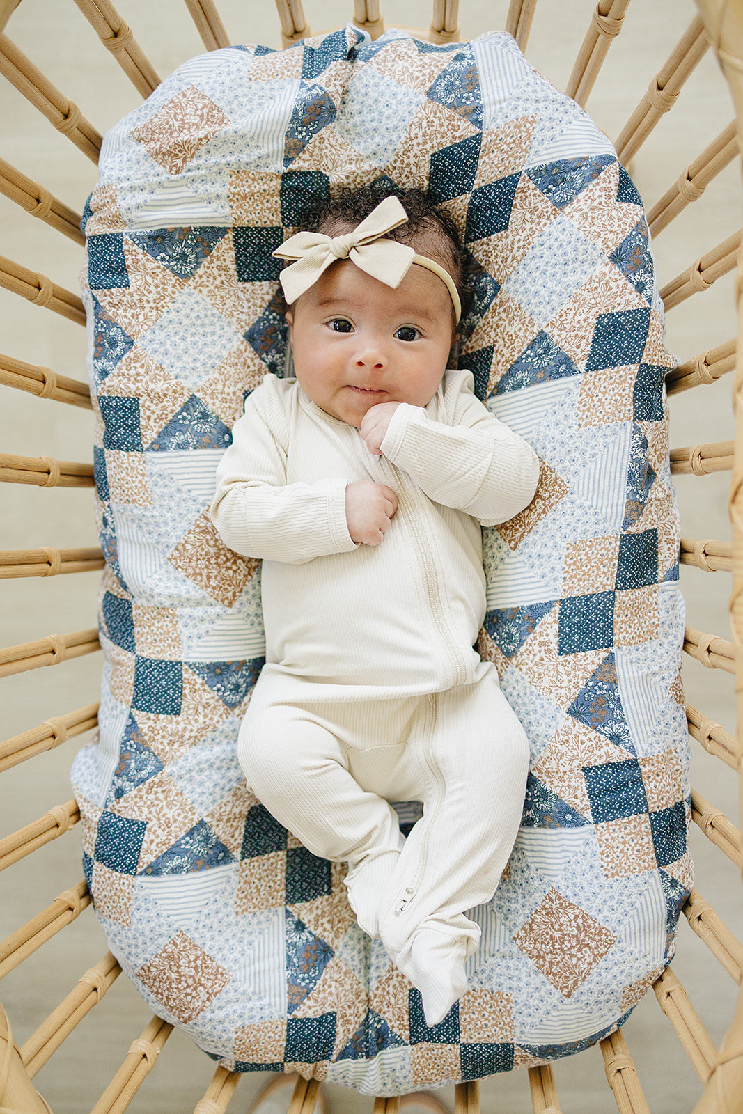 Baby in a white outfit sitting on a textured blanket in a wooden crib