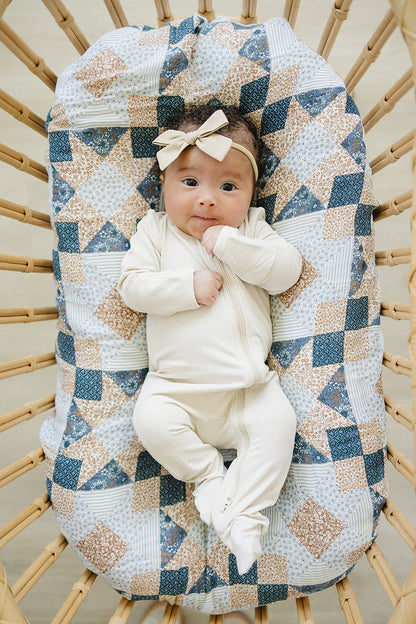 Baby in a white outfit sitting on a textured blanket in a wooden crib
