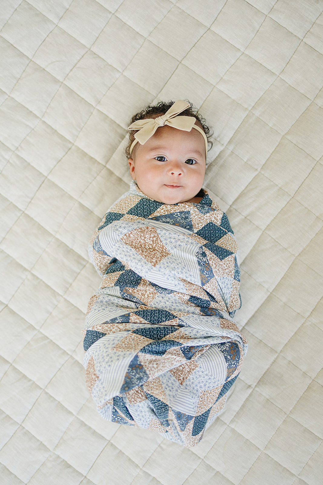 Newborn baby swaddled in a patterned blanket on a textured surface