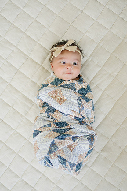 Newborn baby swaddled in a patterned blanket on a textured surface