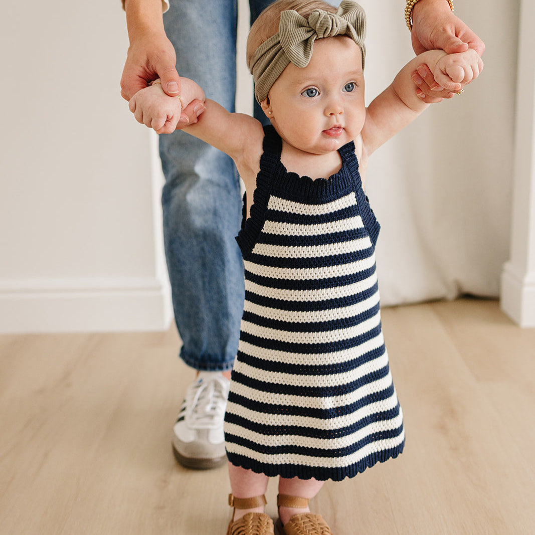 Child in a striped dress holding hands with an adult, both wearing matching outfits.