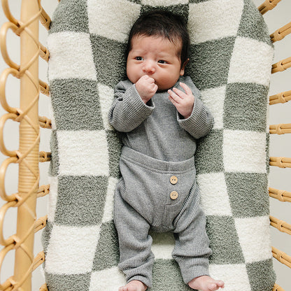 Newborn baby in a gray outfit lying on a checkered blanket in a wicker basket.