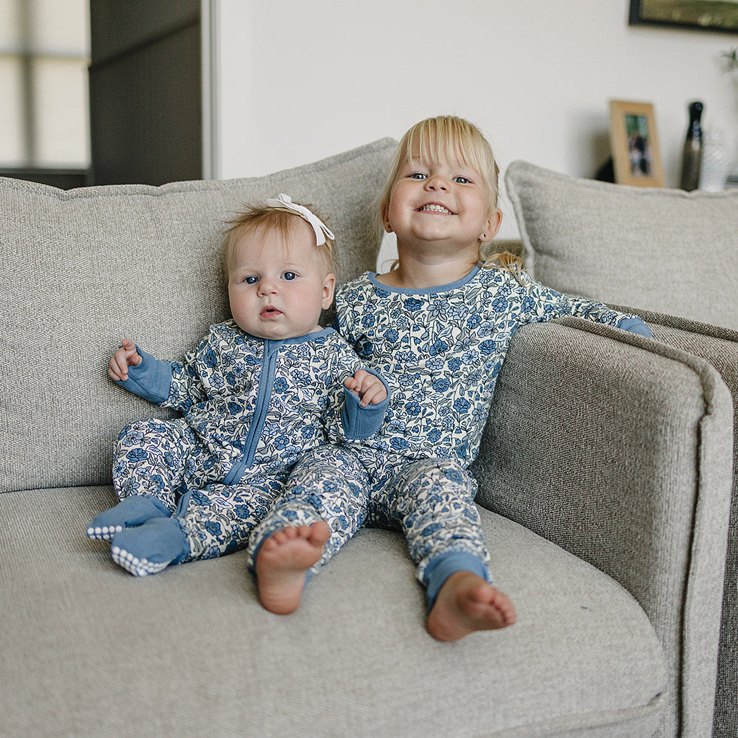 Two children in matching blue and white pajamas sitting on a beige couch.