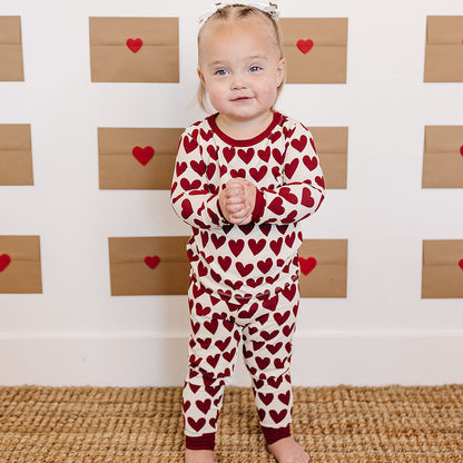 Child wearing a red heart-patterned onesie standing in front of a wall with heart designs.