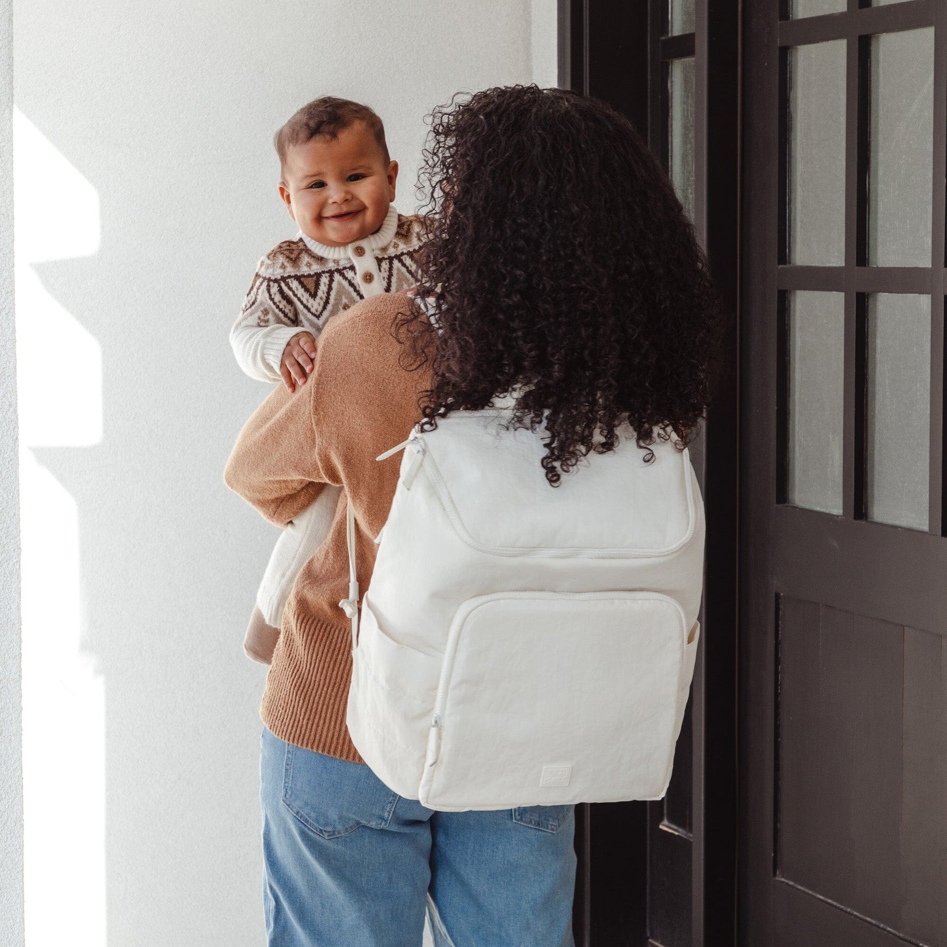 Woman with a white backpack holding a child in a home setting