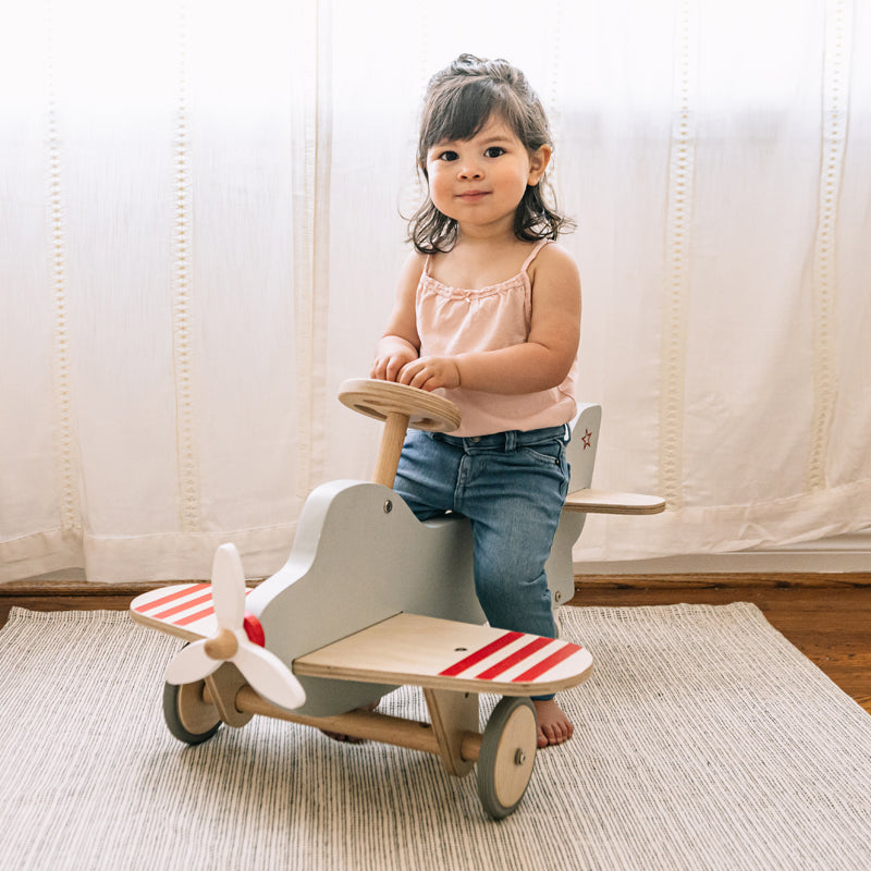 Child playing with a wooden toy airplane indoors