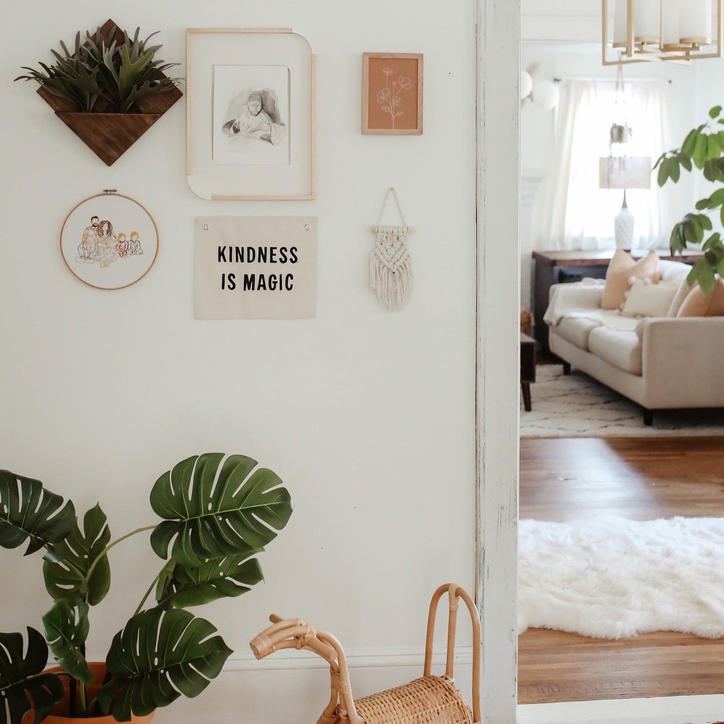 Decorative wall with plants, a sign reading 'Kindness is Magic', and a view into a living room.