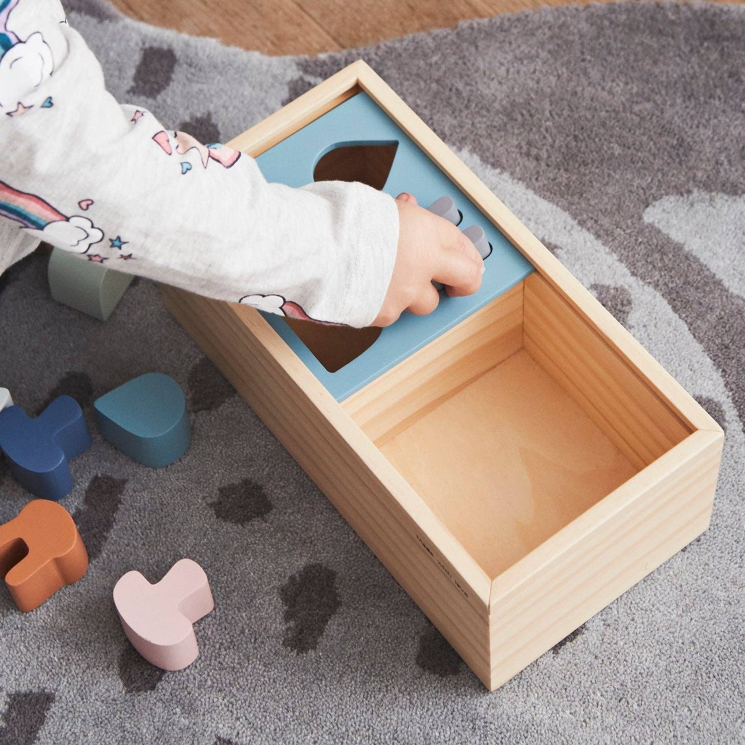 Child playing with a wooden shape sorting toy on a carpeted floor.