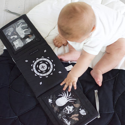 Baby interacting with a black and white patterned book on a bed