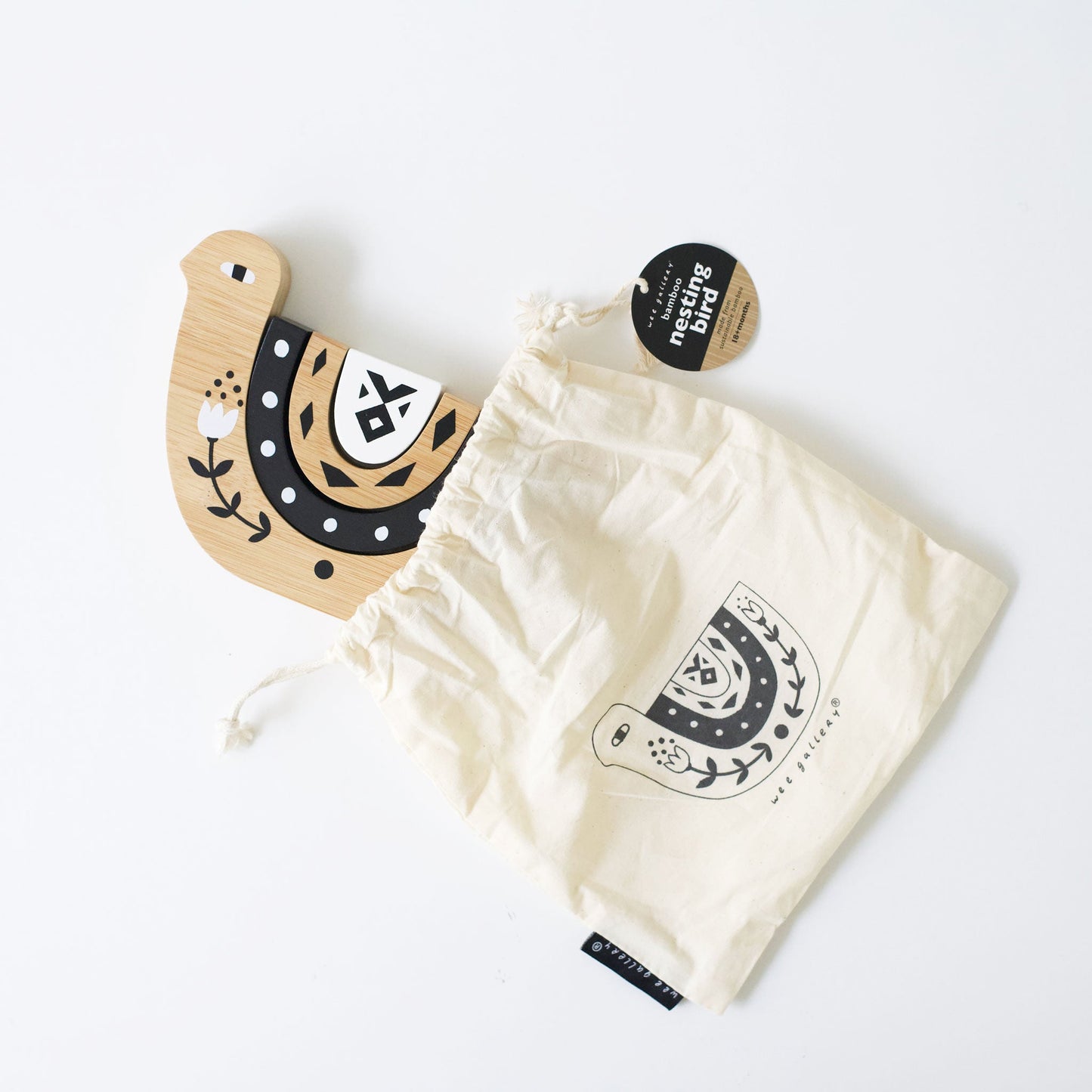 Wooden horseshoe-shaped object with floral design next to a white drawstring bag with a similar design on a light gray background.