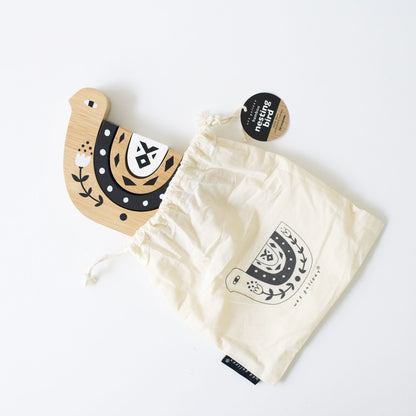 Wooden horseshoe-shaped object with floral design next to a white drawstring bag with a similar design on a light gray background.