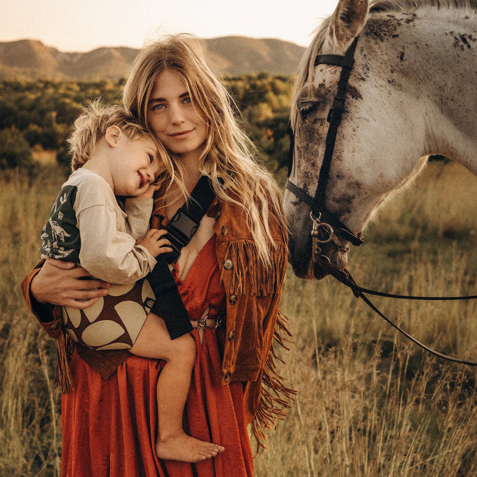 Woman holding a child in a field with a horse