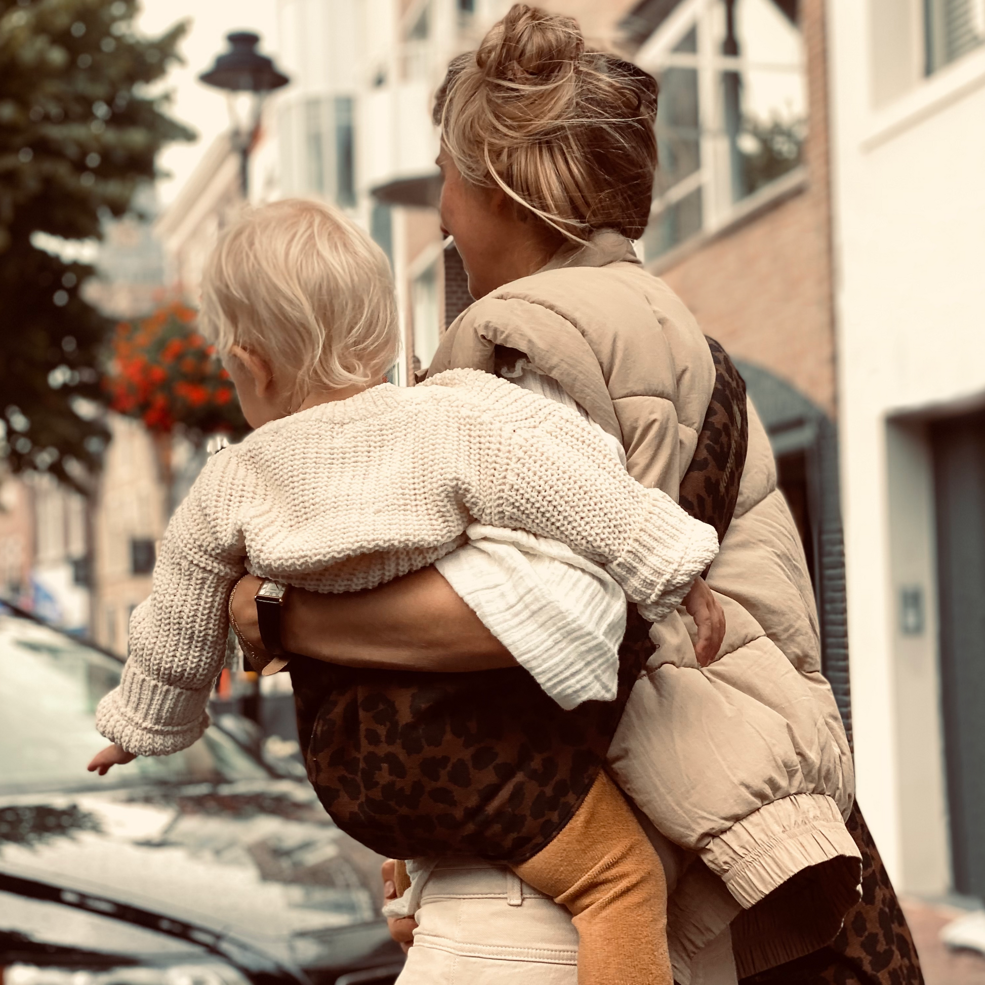 Woman holding a child on a city street with buildings and cars in the background