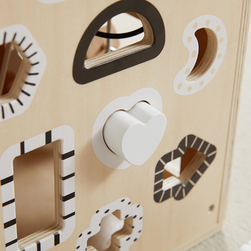 Wooden shape sorting toy with various geometric holes and a white knob on a beige background