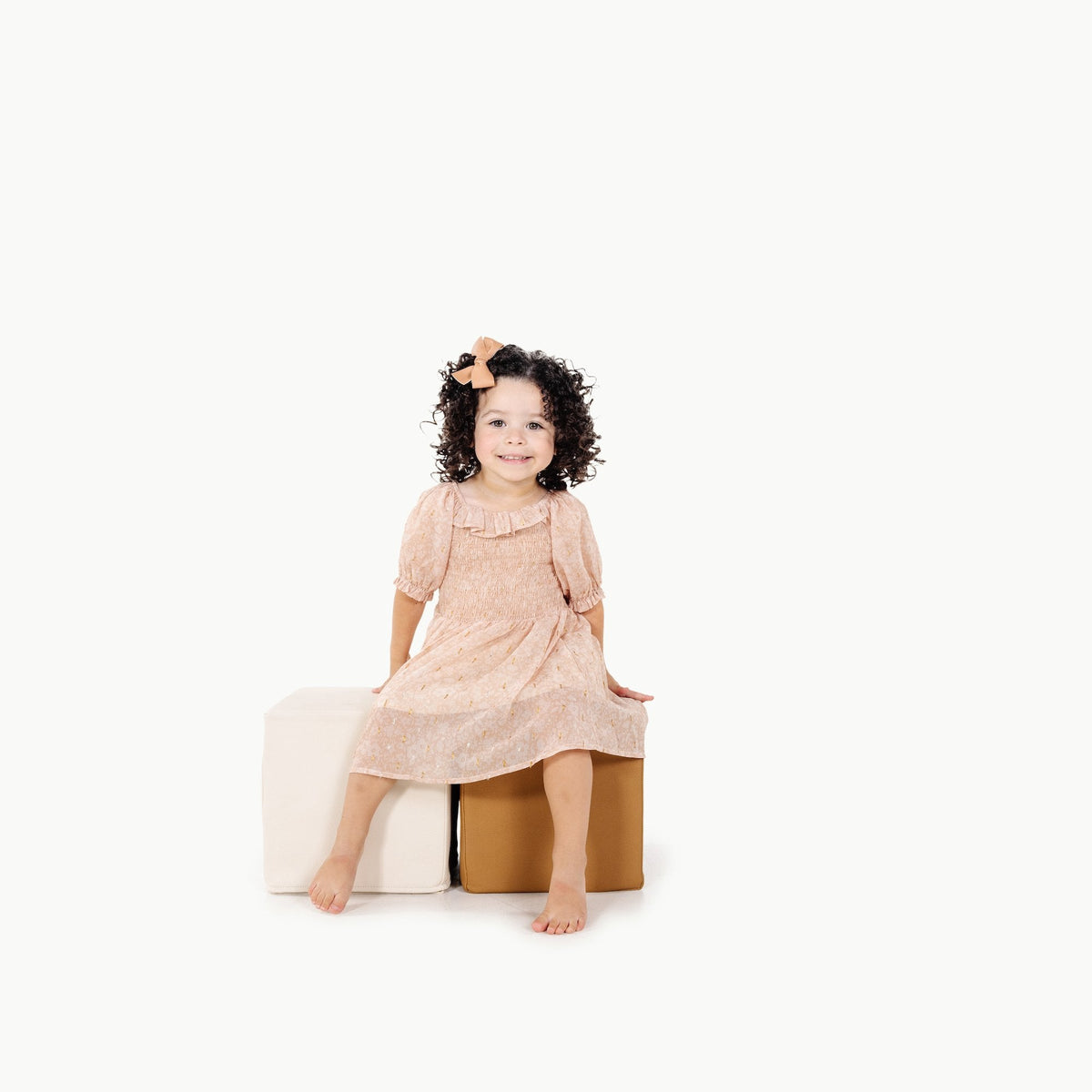 Young girl in a pink dress sitting on a white surface with a white background
