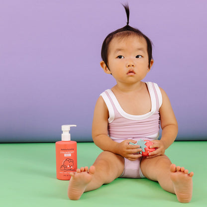 Child sitting on a green floor with a pink bottle and toy, against a purple background
