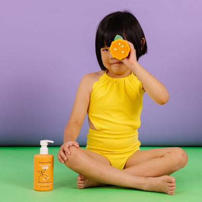 Child in yellow swimsuit holding an orange toy with a bottle of sunscreen on a green and purple background