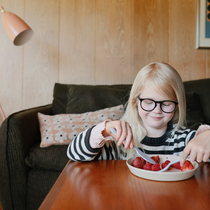 Child with glasses eating strawberries at a table in a cozy living room.
