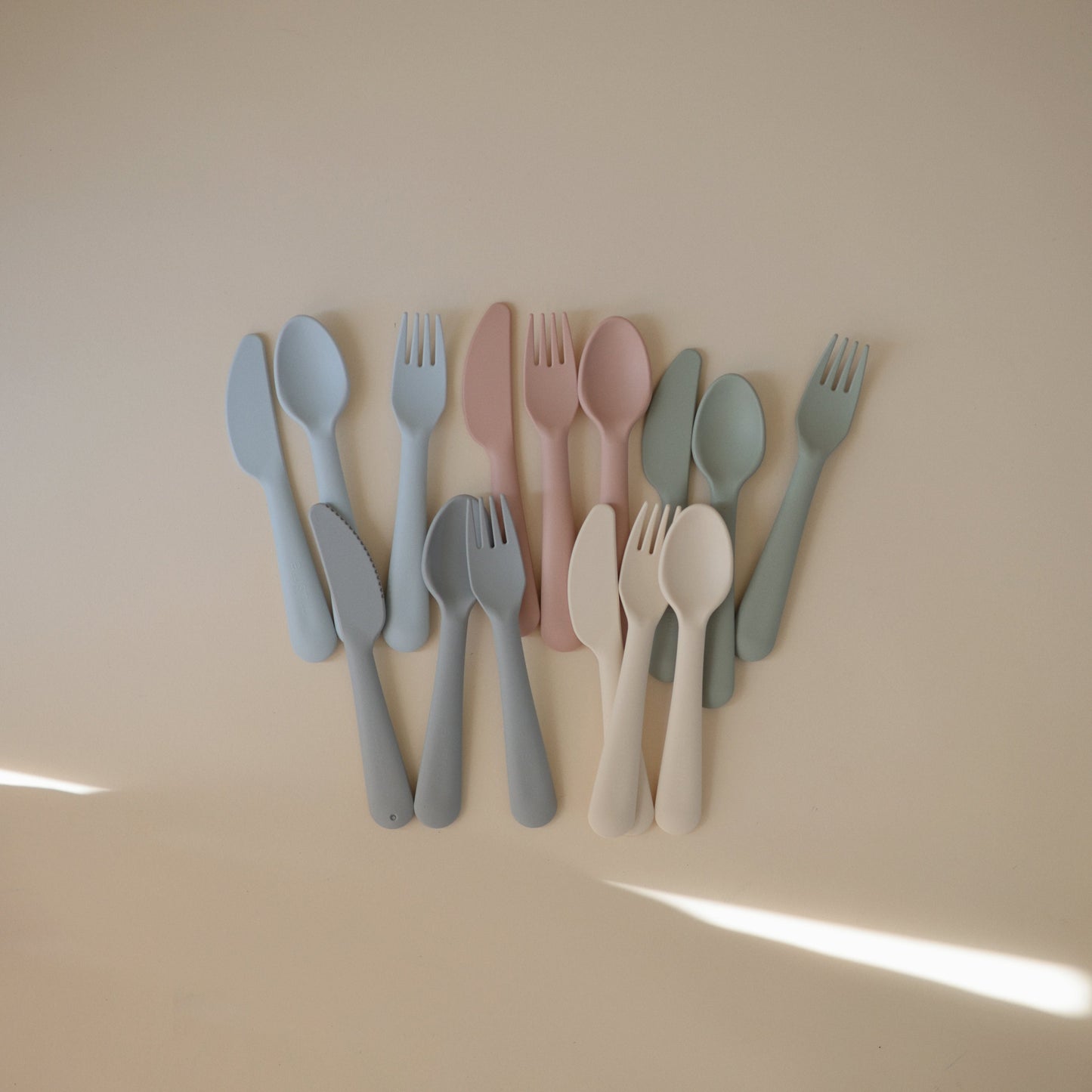 Set of colorful cutlery including knives, forks, and spoons on a beige background