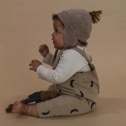 Child wearing a beige romper with black patterns and a matching hat on a beige background