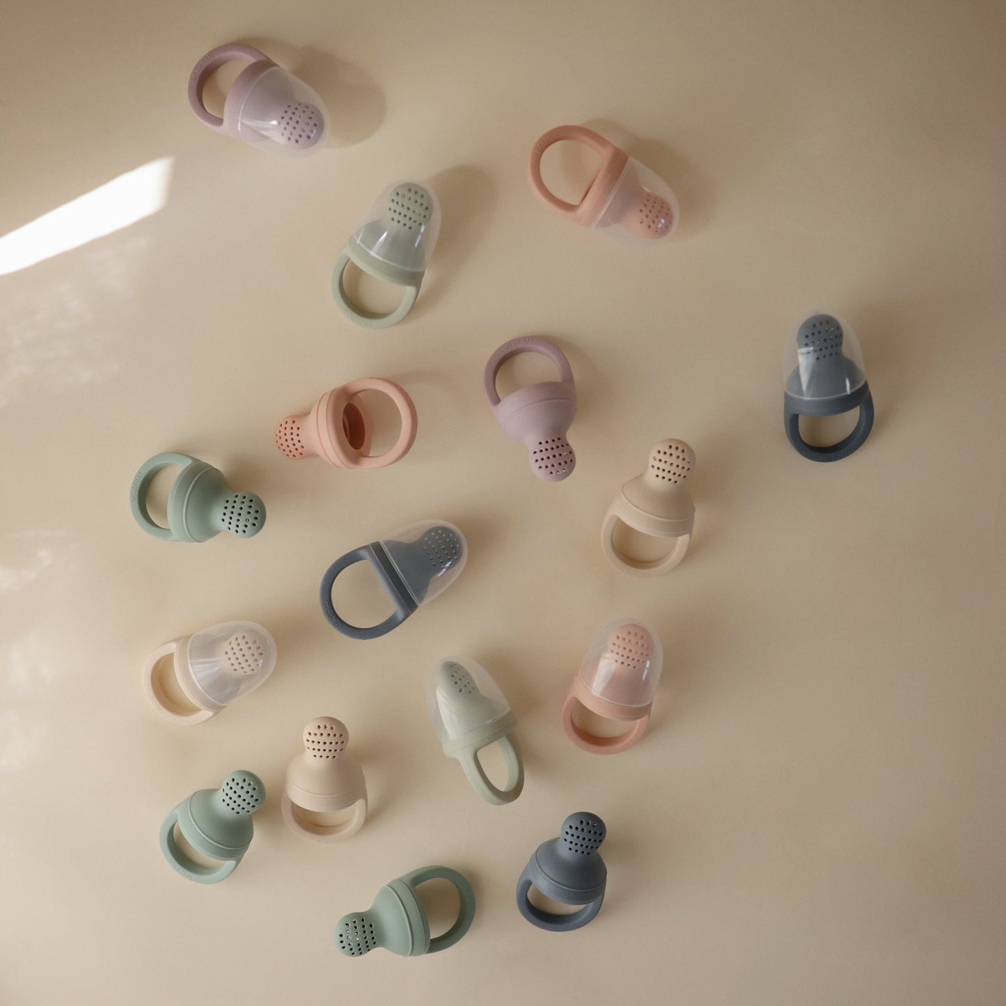 Various silicone baby teething rings in pastel colors on a beige surface.