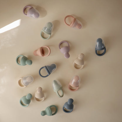 Various silicone baby teething rings in pastel colors on a beige surface.