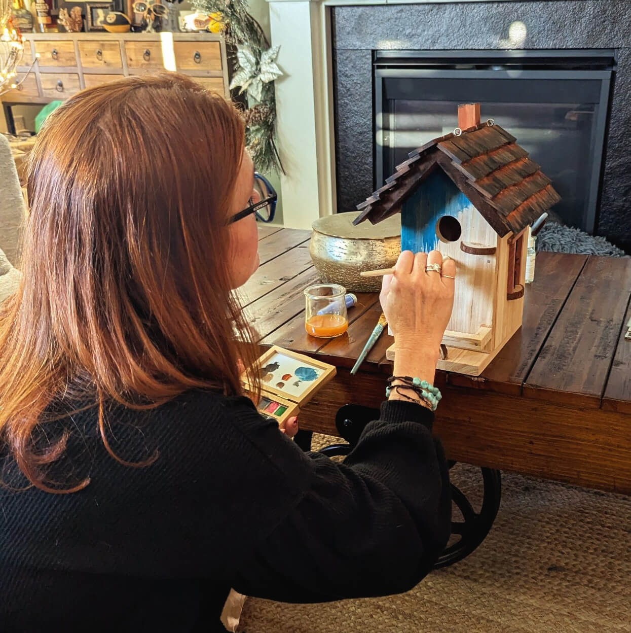 Person painting a wooden birdhouse in a cozy living room.